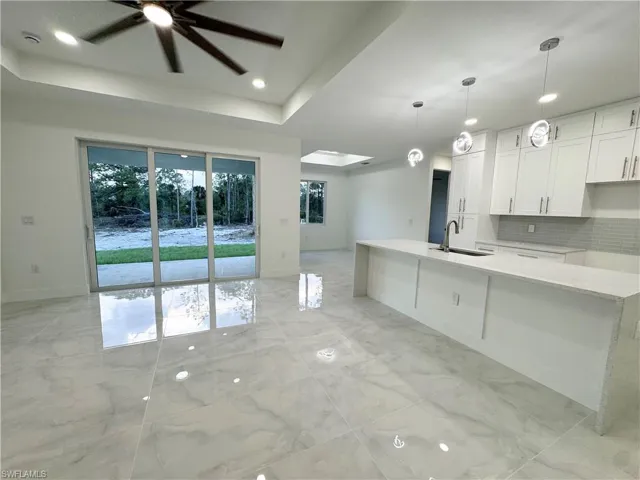 Kitchen featuring a ceiling fan, marble finish floor, baseboards, white cabinetry, and a sink