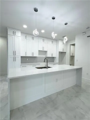 Kitchen featuring white cabinets, a sink, marble finish floor, baseboards, and a large island with sink