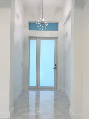 Foyer featuring baseboards, marble finish floor, and a notable chandelier