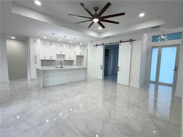 Unfurnished living room with a raised ceiling, recessed lighting, a barn door, and marble finish floor