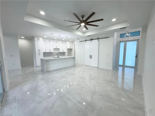 Unfurnished living room with recessed lighting, a barn door, a raised ceiling, and baseboards