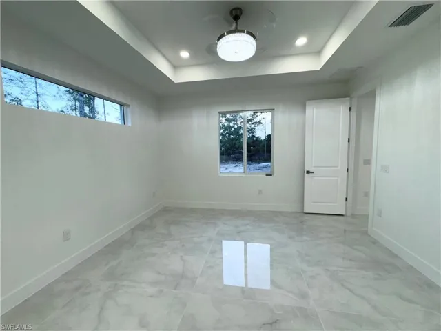 Empty room featuring visible vents, a raised ceiling, marble finish floor, and baseboards