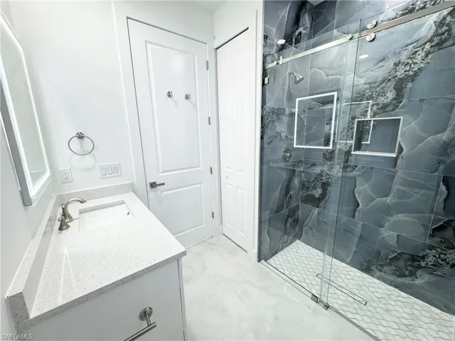 Full bath featuring a marble finish shower, marble finish floor, and vanity