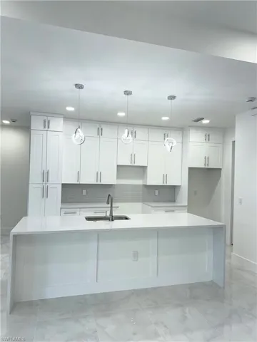 Kitchen with white cabinets, backsplash, a sink, and marble finish floor