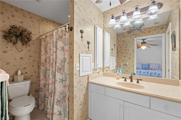 Bathroom featuring curtained shower, vanity, ceiling fan, toilet, and tile patterned floors