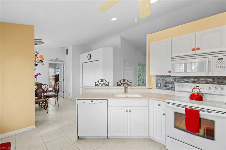 Kitchen featuring vaulted ceiling, sink, white cabinets, kitchen peninsula, and white appliances