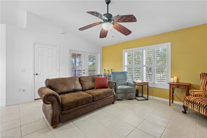 Tiled living room featuring vaulted ceiling, ceiling fan, and french doors