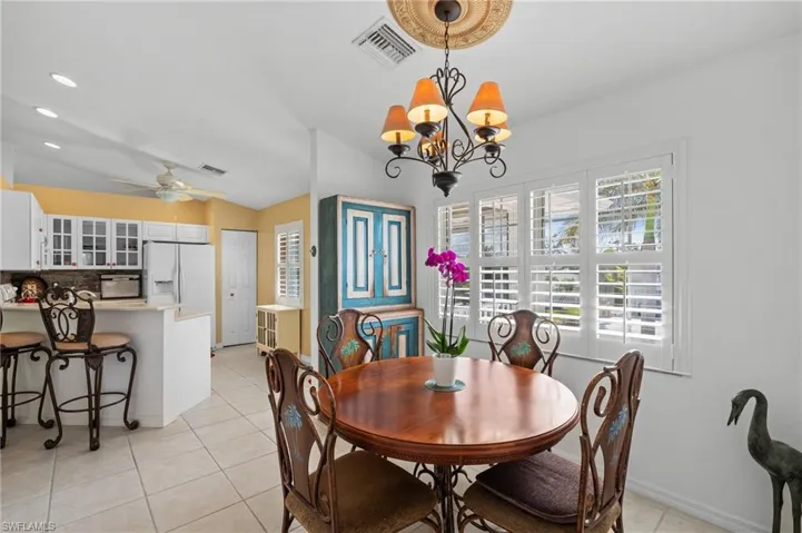 Tiled dining room featuring lofted ceiling and ceiling fan with notable chandelier