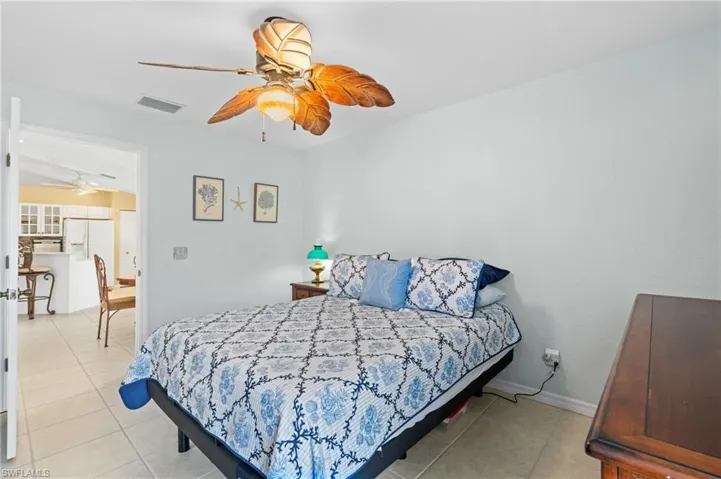 Bedroom with ceiling fan, white refrigerator with ice dispenser, and light tile patterned floors
