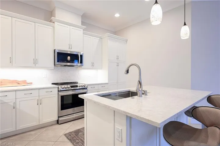 Kitchen with a kitchen island with sink, hanging light fixtures, stainless steel appliances, sink, and white cabinetry