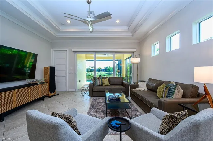 Tiled living room with ceiling fan, a raised ceiling, and ornamental molding
