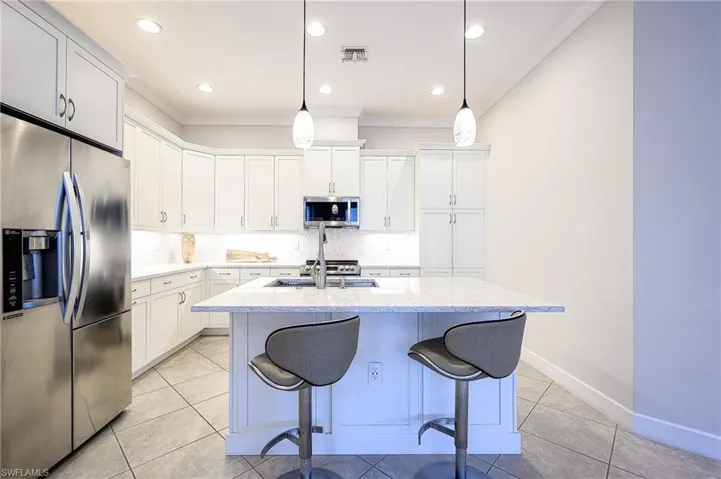 Kitchen with appliances with stainless steel finishes, white cabinetry, a center island with sink, and pendant lighting
