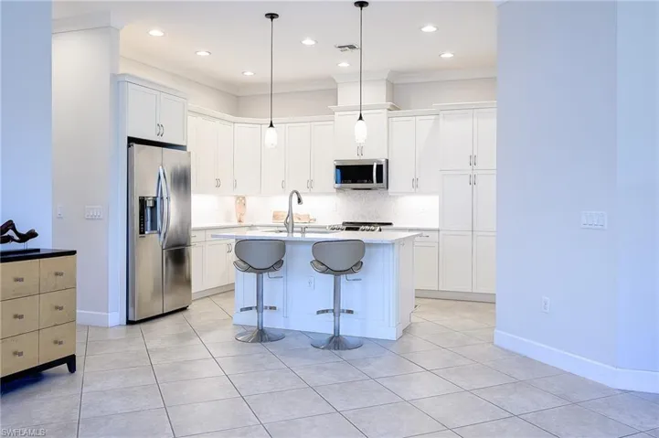 Kitchen featuring a kitchen island with sink, stainless steel appliances, sink, a breakfast bar, and white cabinets