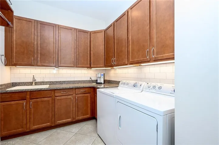 Laundry room featuring washing machine and clothes dryer, cabinets, sink, and light tile patterned flooring