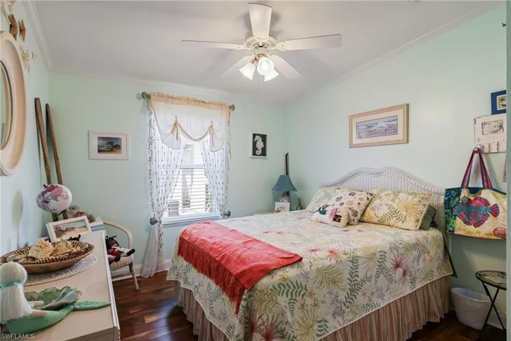 Inviting room featuring wood-finish flooring, a ceiling fan with light fixture, window with blinds and sheer curtains, and crown molding