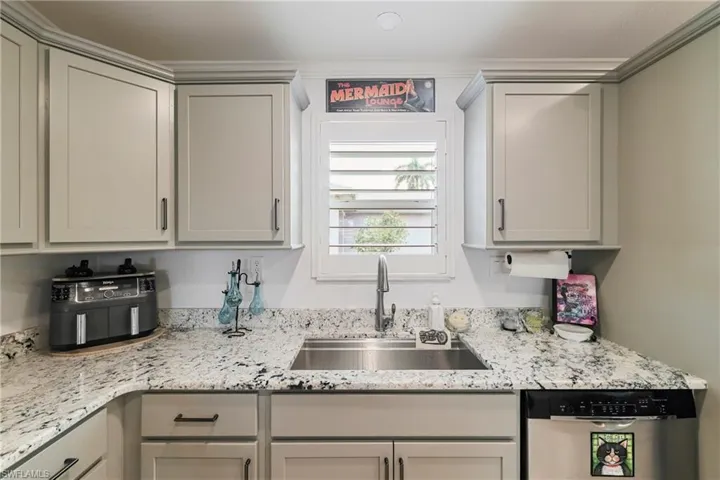 Kitchen featuring light gray shaker-style cabinetry with dark hardware, granite-style countertops, an undermount stainless steel sink with a gooseneck faucet, a window with plantation shutters, and a stainless steel dishwasher