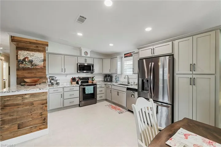 Kitchen featuring light grey cabinetry with brushed nickel hardware, white quartz countertops, stainless steel appliances, and a wood-finish accent wall