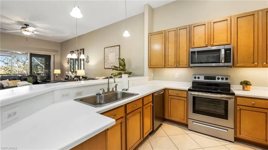 Kitchen with stainless steel appliances, light countertops, wood finish cabinets, a ceiling fan, and open floor plan