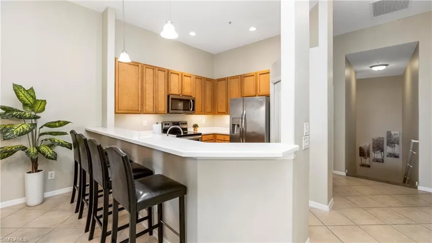 Kitchen featuring stainless steel appliances, light countertops, decorative light fixtures, light tile patterned flooring, and a kitchen bar