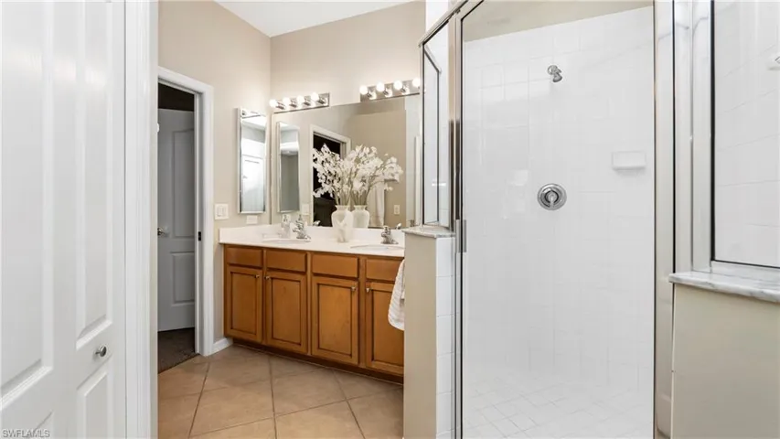 Bathroom featuring double vanity, a shower stall, and light tile patterned flooring