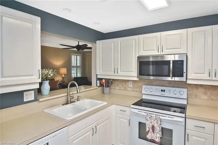 Kitchen with a sink, light countertops, white appliances, and white cabinetry