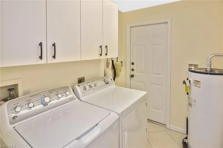 Laundry room featuring cabinet space, light tile patterned floors, baseboards, water heater, and washer and dryer