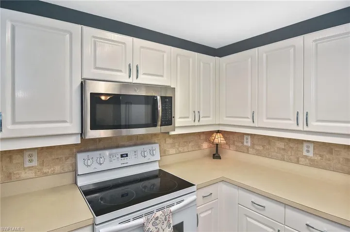 Kitchen with electric range, light countertops, stainless steel microwave, white cabinets, and backsplash