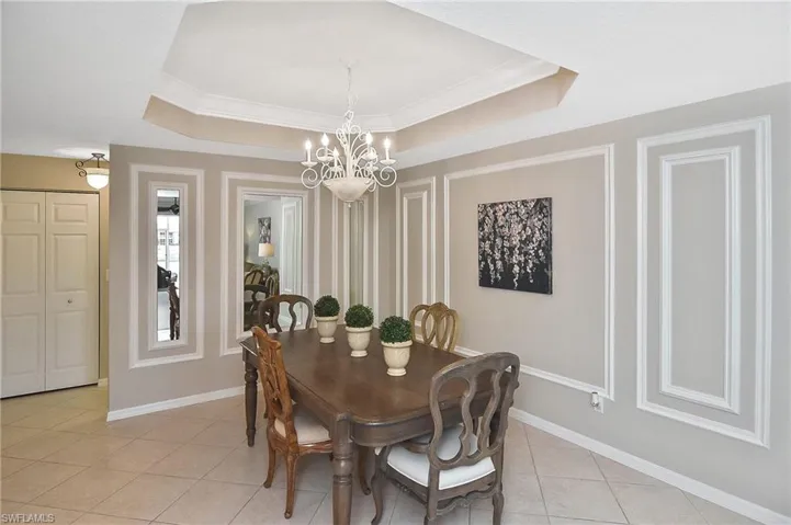 Dining room with baseboards, a tray ceiling, light tile patterned floors, and a chandelier