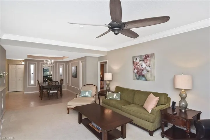 Living area featuring ornamental molding, light tile patterned flooring, light carpet, baseboards, and ceiling fan with notable chandelier