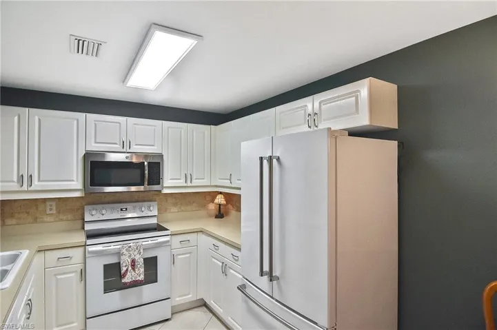 Kitchen with white appliances, white cabinetry, visible vents, and light countertops