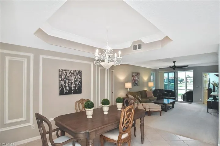 Dining room with visible vents, ornamental molding, light colored carpet, a tray ceiling, and light tile patterned floors