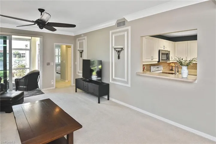Living area with ceiling fan, light carpet, baseboards, visible vents, and ornamental molding