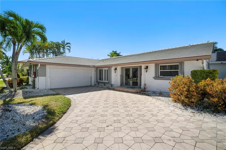 Single story home featuring a garage, stucco siding, french doors, and decorative driveway