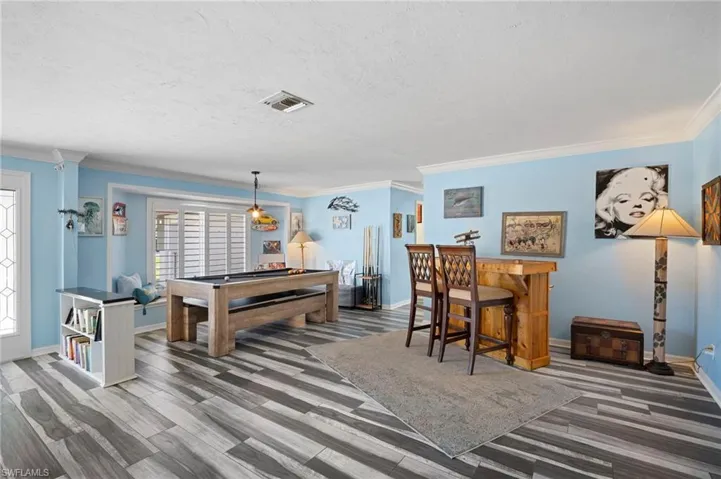 Game room featuring pool table, ornamental molding, light wood-style flooring, a dry bar, and a textured ceiling