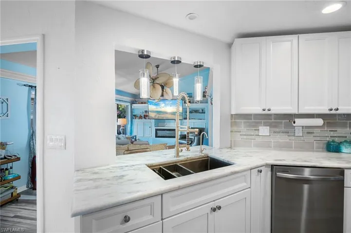 Kitchen with white cabinetry, dishwasher, decorative backsplash, light stone counters, and wood finished floors