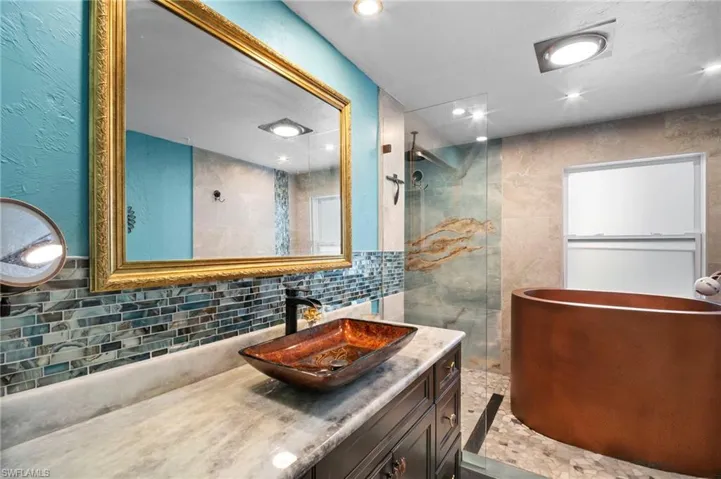 Bathroom featuring vanity, a walk in shower, backsplash, recessed lighting, and tile walls