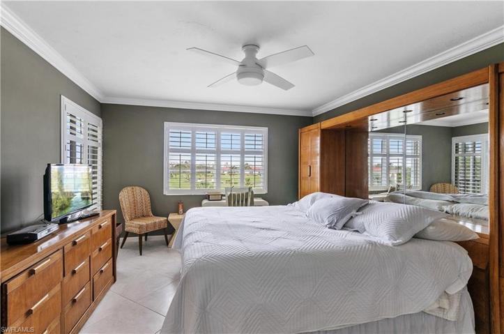 Master bedroom with extra storage, crown molding, tile floors, newer fan/light, plantation shutters, siding door to the lanai.