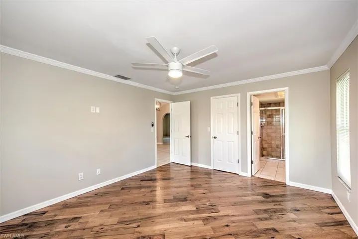 Unfurnished bedroom featuring ensuite bath, crown molding, ceiling fan, and wood-type flooring