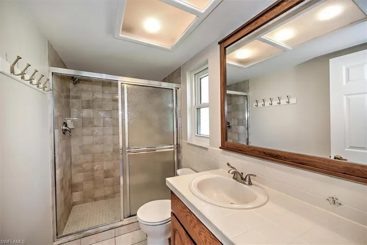 Bathroom featuring a shower with shower door, toilet, vanity, tile patterned floors, and decorative backsplash
