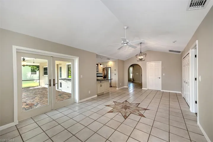 Unfurnished living room with lofted ceiling, ceiling fan with notable chandelier, french doors, and light tile patterned floors