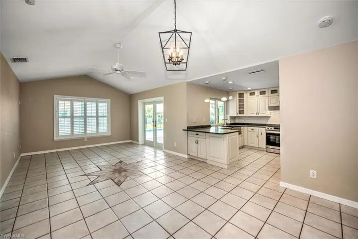 Kitchen with light tile patterned flooring, pendant lighting, stainless steel stove, vaulted ceiling, and backsplash