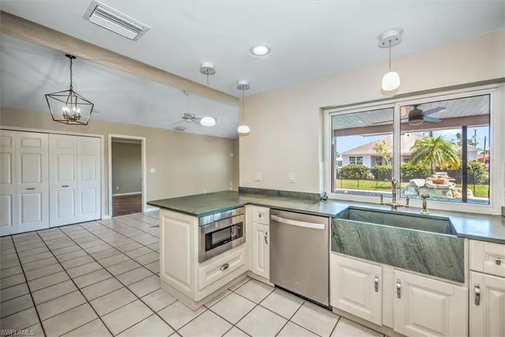 Kitchen with stainless steel appliances, kitchen peninsula, decorative light fixtures, ceiling fan with notable chandelier, and light tile patterned flooring