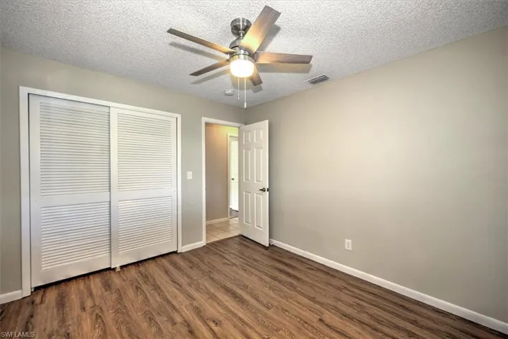 Unfurnished bedroom with a textured ceiling, a closet, wood-type flooring, and ceiling fan