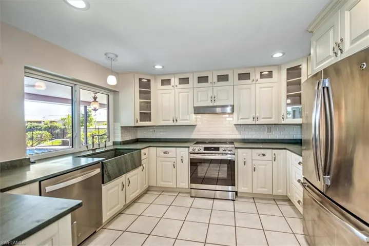 Kitchen featuring tasteful backsplash, light tile patterned floors, appliances with stainless steel finishes, decorative light fixtures, and sink
