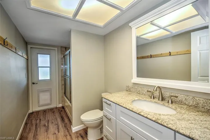 Full bathroom featuring vanity, hardwood / wood-style flooring, bath / shower combo with glass door, and toilet