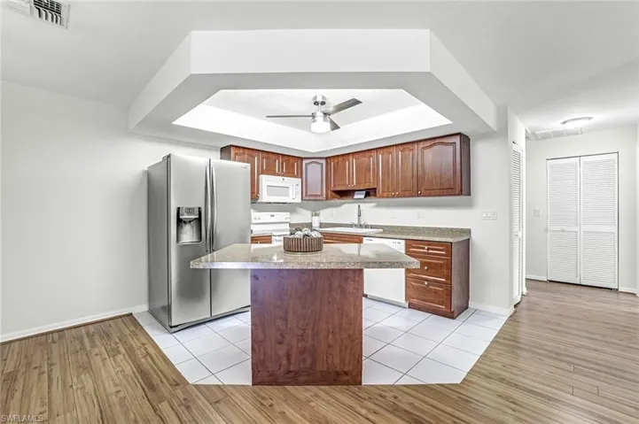 Kitchen with white appliances, light wood-type flooring, a center island, and baseboards