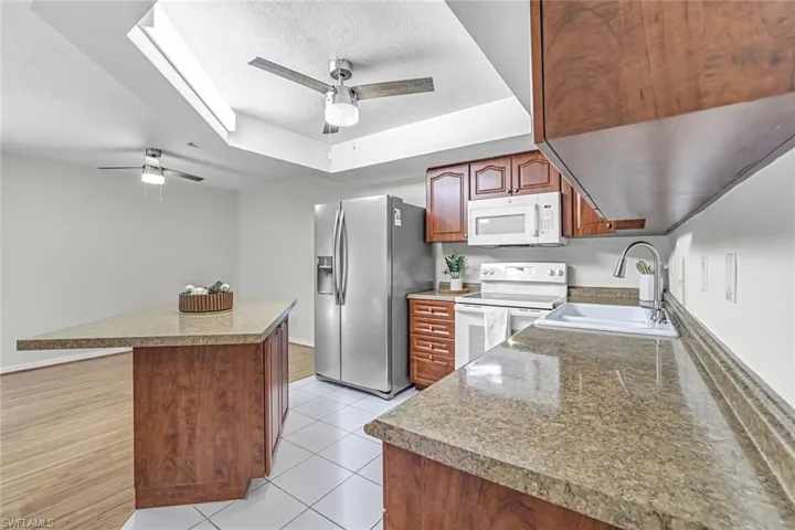 Kitchen featuring white appliances, a sink, a ceiling fan, a raised ceiling, and a textured ceiling