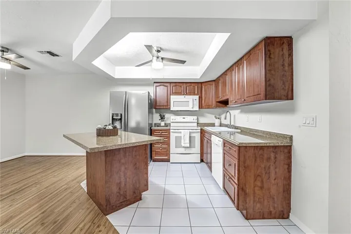 Kitchen with white appliances, ceiling fan, a sink, a tray ceiling, and a kitchen island