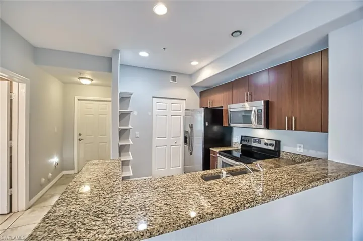 Kitchen with kitchen peninsula, sink, stainless steel appliances, stone counters, and light tile patterned flooring