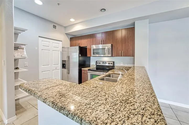 Kitchen featuring light stone countertops, stainless steel appliances, kitchen peninsula, and sink
